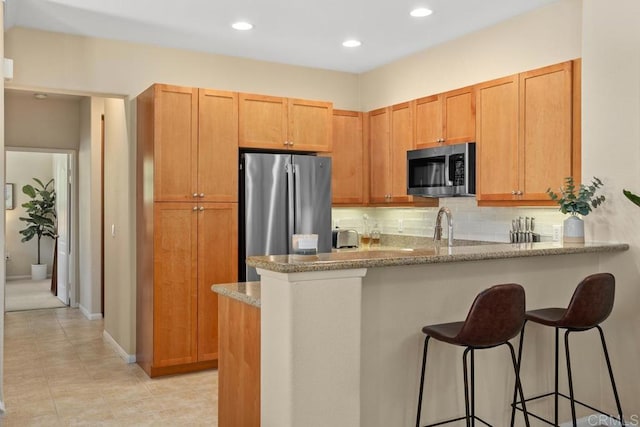12737 Savannah Creek Dr Unit 280, San Diego, CA 92128 - kitchen with appliances with stainless steel finishes, a breakfast bar area, a peninsula, tasteful backsplash, and light stone countertops