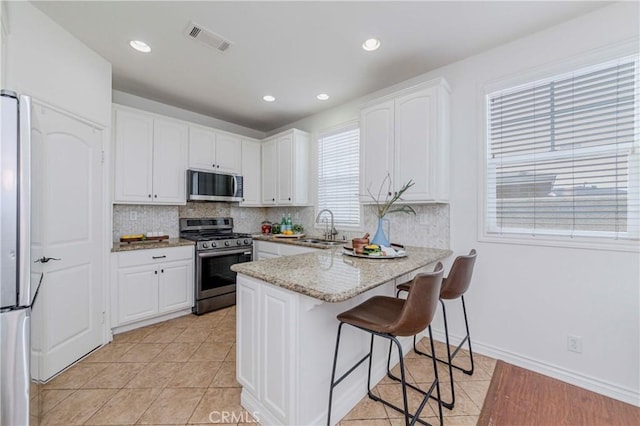 8647 Belmont St, Cypress, CA 90630 - kitchen featuring stainless steel appliances, a peninsula, white cabinets, tasteful backsplash, and a breakfast bar