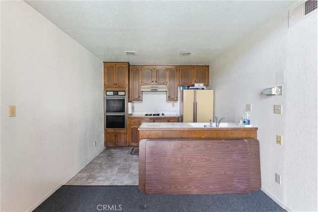 7625 Reseda Blvd Unit 302, Reseda, CA 91335 - kitchen featuring black appliances, a peninsula, under cabinet range hood, a textured wall, and brown cabinetry