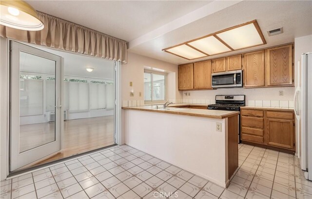 1144 Jasmine St, Redlands, CA 92374 - kitchen featuring stainless steel appliances, light countertops, a peninsula, and brown cabinetry