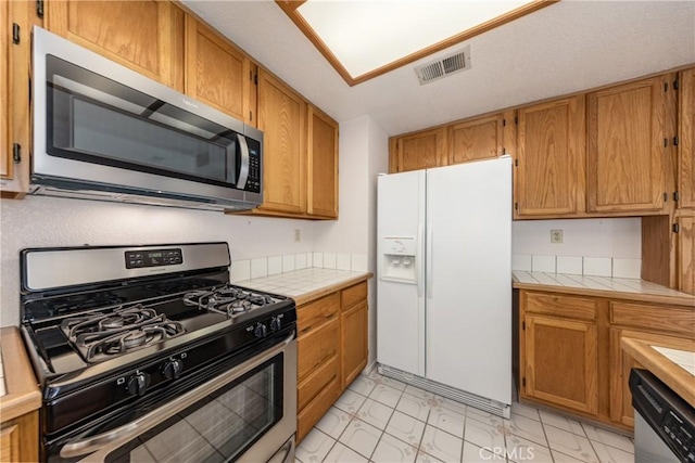 1144 Jasmine St, Redlands, CA 92374 - kitchen featuring stainless steel appliances, tile countertops, light marble finish floors, and brown cabinets