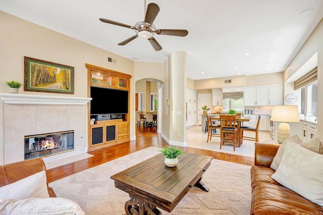 282 Camino Del Postigo, Escondido, CA 92029 - living area with arched walkways, light wood finished floors, a tiled fireplace, a ceiling fan, and recessed lighting