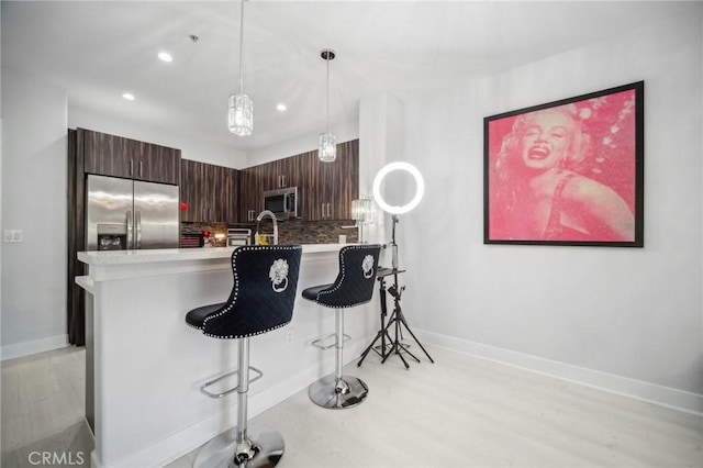 24545 Town Center Dr Unit 5405, Valencia, CA 91355 - kitchen featuring stainless steel appliances, light wood-style flooring, a breakfast bar area, decorative backsplash, and light countertops