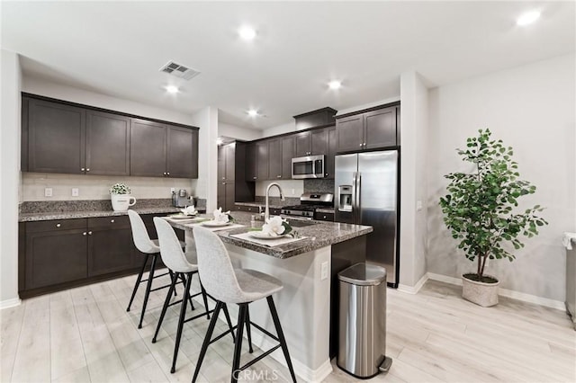 16502 Casa Grande Ave Unit 318, Fontana, CA 92336 - kitchen featuring appliances with stainless steel finishes, light wood finished floors, dark brown cabinetry, a breakfast bar, and a kitchen island with sink