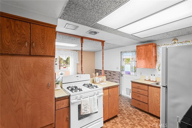 27439 Santa Clarita Rd, Saugus, CA 91350 - kitchen with gas range gas stove, freestanding refrigerator, light countertops, and brown cabinetry
