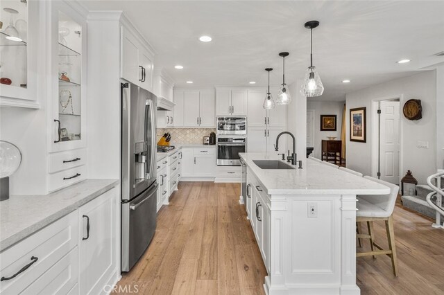 21891 Winnebago Ln, Lake Forest, CA 92630 - kitchen with stainless steel appliances, a breakfast bar area, white cabinets, light wood-type flooring, and decorative backsplash
