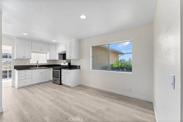 558 W Philadelphia St, Ontario, CA 91762 - kitchen featuring stainless steel gas range, dark countertops, light wood-type flooring, under cabinet range hood, and white cabinetry