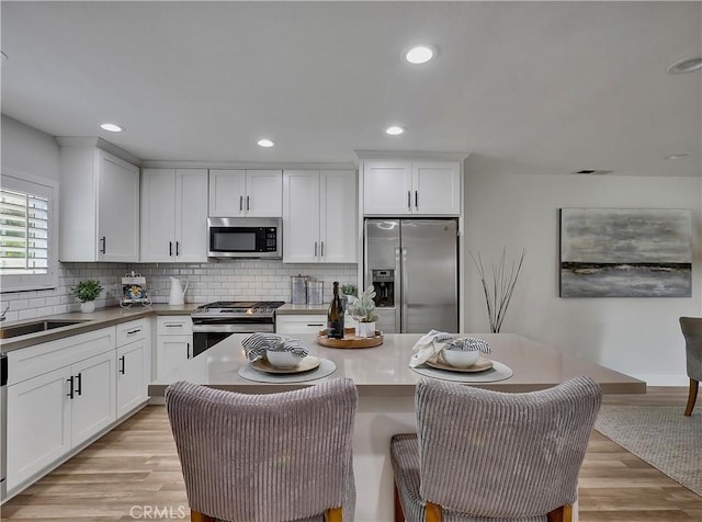 2867 Turnbull St, Oceanside, CA 92054 - kitchen featuring stainless steel appliances, decorative backsplash, white cabinetry, light wood-style flooring, and a center island