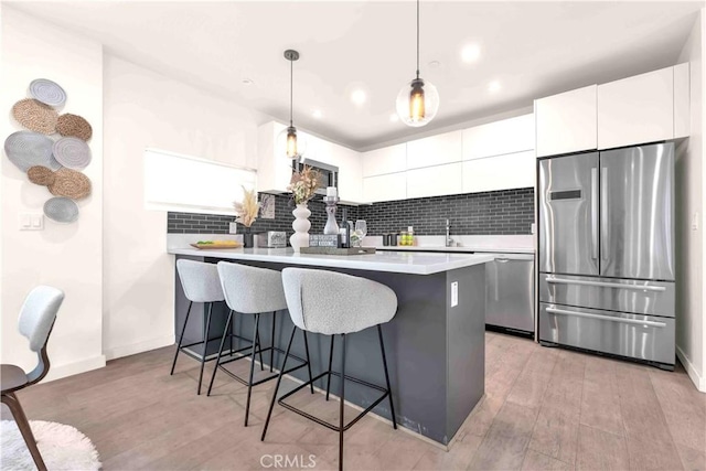 1131/2 N Manhattan Pl, Los Angeles, CA 90004 - kitchen with stainless steel appliances, a breakfast bar, backsplash, light countertops, and white cabinets
