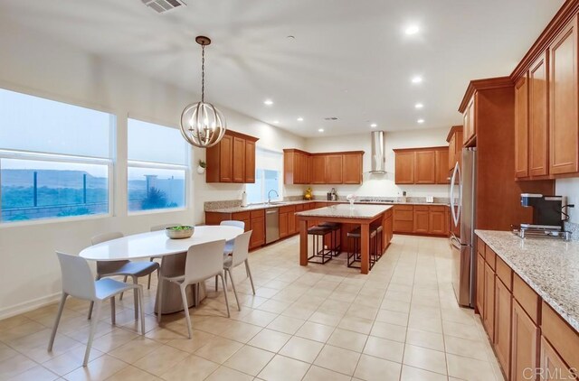 1873 El Paseo Ave, Chula Vista, CA 91913 - kitchen featuring wall chimney range hood, stainless steel appliances, brown cabinets, a breakfast bar area, and light stone counters