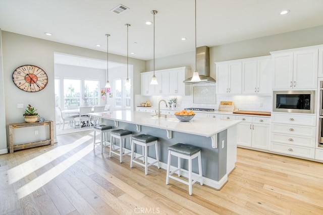 916 Trail View Pl, Nipomo, CA 93444 - kitchen with wall chimney exhaust hood, built in microwave, light wood finished floors, a breakfast bar, and recessed lighting