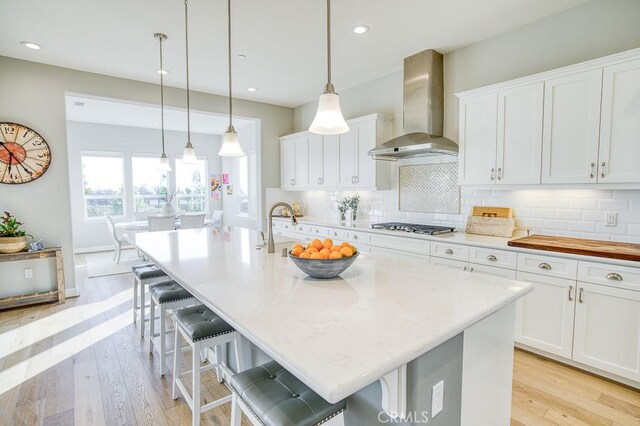 916 Trail View Pl, Nipomo, CA 93444 - kitchen featuring wall chimney exhaust hood, stainless steel gas stovetop, tasteful backsplash, white cabinetry, and light wood-type flooring