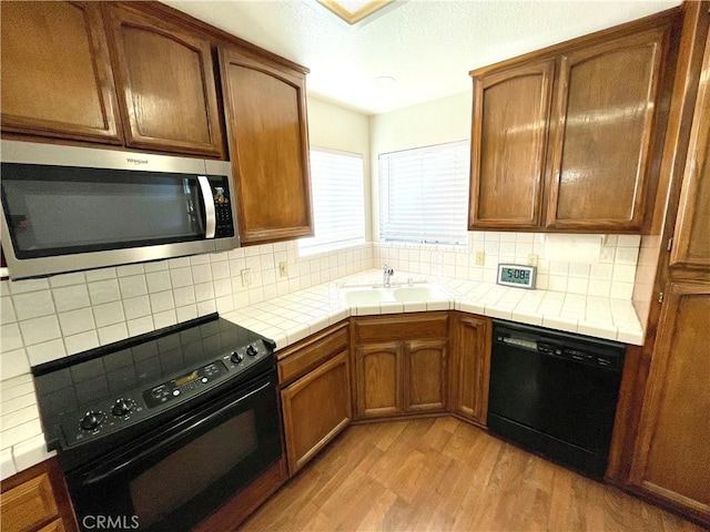 659 Royal Arch Ct, Merced, CA 95340 - kitchen with black appliances, light wood-style flooring, tile countertops, and decorative backsplash