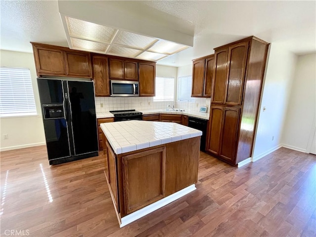 659 Royal Arch Ct, Merced, CA 95340 - kitchen featuring black appliances, backsplash, tile countertops, a center island, and light wood finished floors