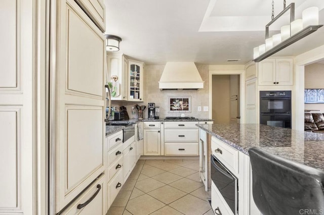 26267 Bellemore Dr, Ramona, CA 92065 - kitchen featuring custom exhaust hood, light tile patterned floors, glass insert cabinets, cream cabinetry, and stainless steel gas stovetop
