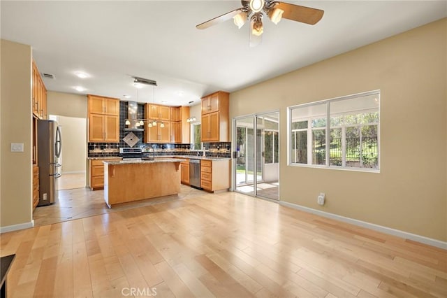 33087 Corte Ganso, Temecula, CA 92592 - kitchen with stainless steel appliances, decorative backsplash, a center island with sink, ceiling fan, and light wood-style floors