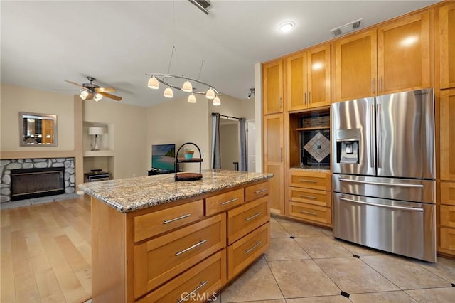 33087 Corte Ganso, Temecula, CA 92592 - kitchen with stainless steel refrigerator with ice dispenser, a stone fireplace, light stone countertops, a center island, and a ceiling fan