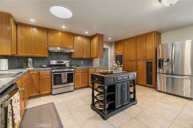 7 Calgary Ln, Chico, CA 95926 - kitchen with stainless steel appliances, under cabinet range hood, brown cabinetry, light tile patterned floors, and decorative backsplash