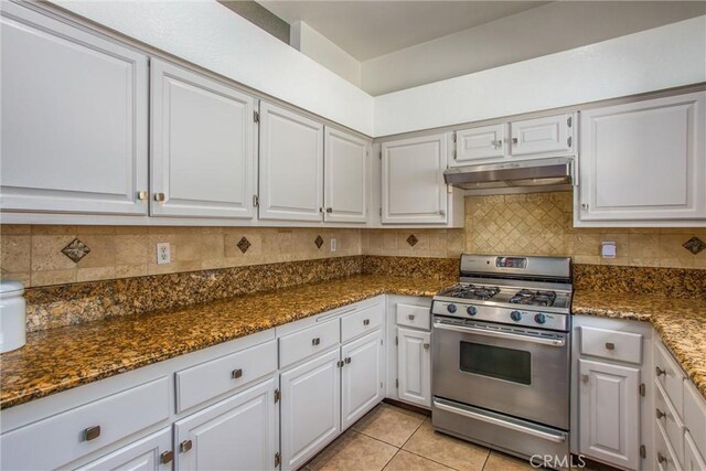 26490 Mapleridge Way, Moreno Valley, CA 92555 - kitchen with stainless steel gas range, under cabinet range hood, white cabinetry, decorative backsplash, and dark stone countertops