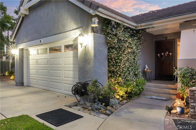 12528 Sonora Way, Victorville, CA 92392 - exterior entry at dusk featuring a garage, stucco siding, and driveway