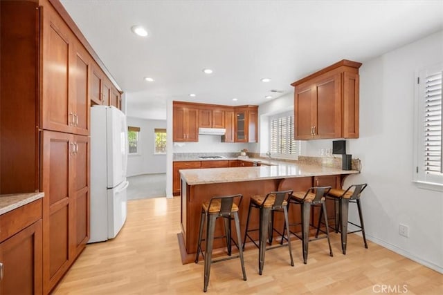 247 Oakwood Ct, Arroyo Grande, CA 93420 - kitchen featuring freestanding refrigerator, a peninsula, under cabinet range hood, light wood finished floors, and brown cabinets