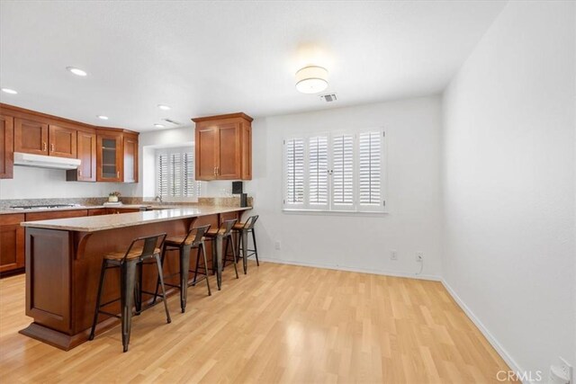 247 Oakwood Ct, Arroyo Grande, CA 93420 - kitchen featuring under cabinet range hood, light wood-style floors, a kitchen bar, light countertops, and recessed lighting