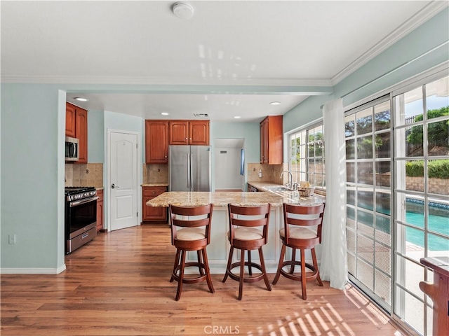 22905 Las Mananitas Dr, Valencia, CA 91354 - kitchen featuring appliances with stainless steel finishes, ornamental molding, a peninsula, light wood-type flooring, and backsplash