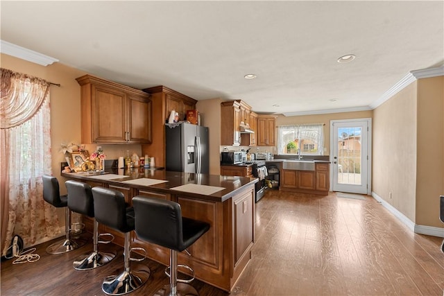 2730 Hayes Ave, Long Beach, CA 90810 - kitchen with stainless steel appliances, a peninsula, wood finished floors, brown cabinetry, and ornamental molding