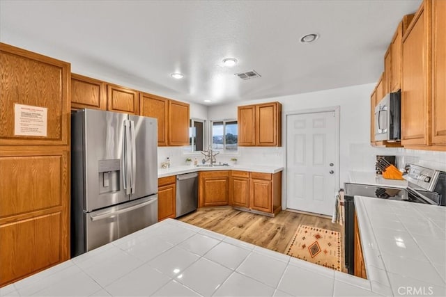 3715 Surrey, Yucca Valley, CA 92284 - kitchen featuring appliances with stainless steel finishes, tile countertops, brown cabinets, backsplash, and light wood-style flooring