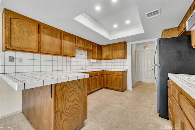 204 Hawk Ln, Palmdale, CA 93551 - kitchen with a raised ceiling, brown cabinetry, backsplash, freestanding refrigerator, and a peninsula
