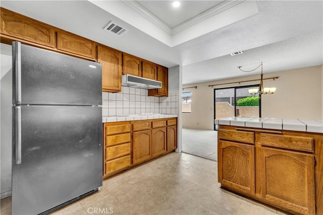 204 Hawk Ln, Palmdale, CA 93551 - kitchen with freestanding refrigerator, under cabinet range hood, crown molding, brown cabinets, and tasteful backsplash