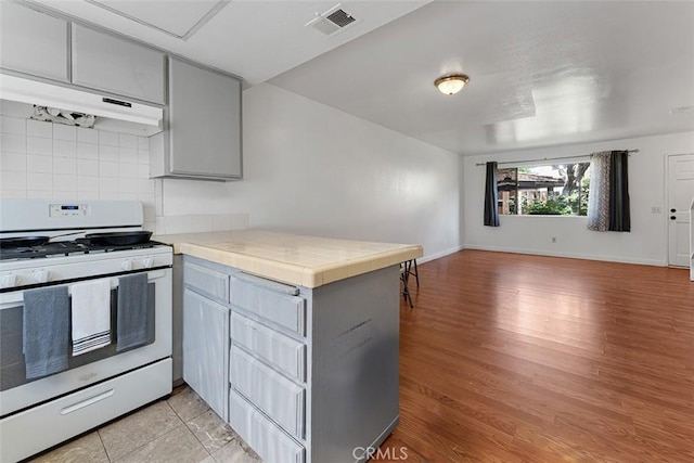 1553 Dennis Pl, West Covina, CA 91790 - kitchen with white gas range, under cabinet range hood, a peninsula, gray cabinetry, and decorative backsplash