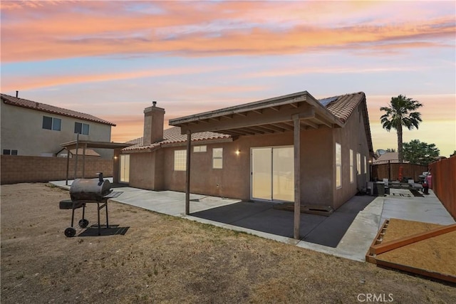 12671 Shorewood Ln, Victorville, CA 92392 - back of property at dusk featuring a tile roof, a fenced backyard, a chimney, a patio area, and stucco siding