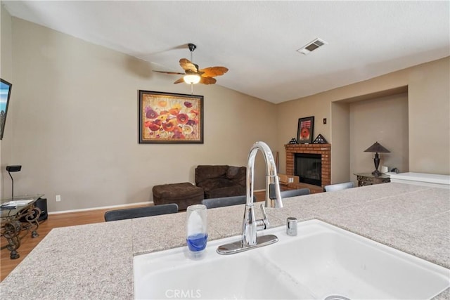 12671 Shorewood Ln, Victorville, CA 92392 - kitchen with wood finished floors, a brick fireplace, a ceiling fan, open floor plan, and light countertops