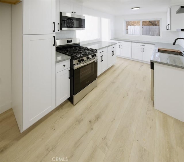 14163 Wimbleton Dr, Victorville, CA 92395 - kitchen with stainless steel appliances, light wood-style flooring, light stone countertops, white cabinets, and decorative backsplash