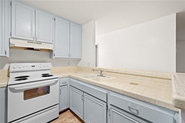 4647 Pico St Unit 101, San Diego, CA 92109 - kitchen with white electric stove, under cabinet range hood, tile counters, gray cabinets, and light wood finished floors
