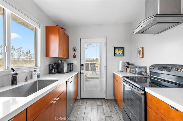 2654 Olympic Rd, Joshua Tree, CA 92252 - kitchen featuring appliances with stainless steel finishes, wall chimney range hood, light countertops, and brown cabinetry