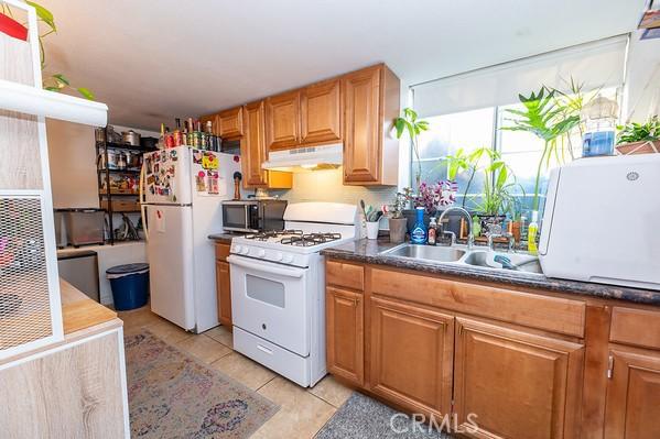 1186 Buelah Ave, City Terrace, CA 90063 - kitchen with white appliances, under cabinet range hood, light tile patterned floors, dark countertops, and brown cabinetry