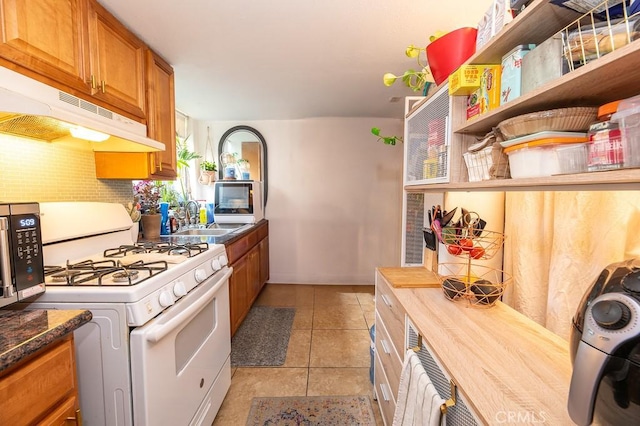 1186 Buelah Ave, City Terrace, CA 90063 - kitchen featuring white range with gas stovetop, under cabinet range hood, brown cabinets, stainless steel microwave, and light tile patterned floors