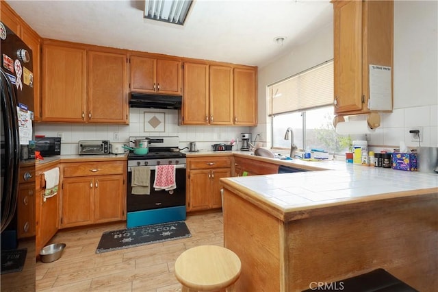 2508 Starbrite Ave, Rosamond, CA 93560 - kitchen featuring gas range, under cabinet range hood, decorative backsplash, a peninsula, and brown cabinets