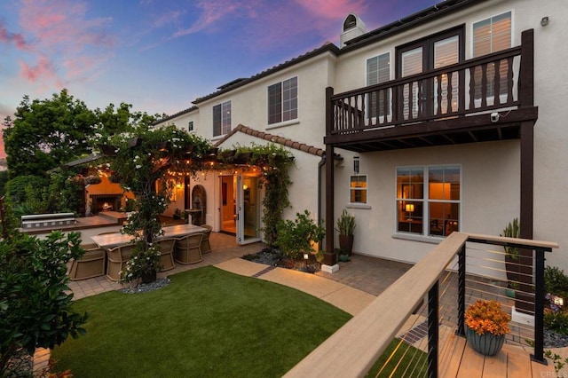 7691 Circulo Sequoia, Carlsbad, CA 92009 - back of house at dusk with a balcony, stucco siding, a lit fireplace, and a lawn