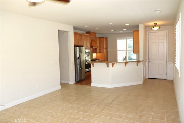 1573 Maple Valley St, Manteca, CA 95336 - kitchen featuring stainless steel appliances, a peninsula, a kitchen bar, premium range hood, and brown cabinets