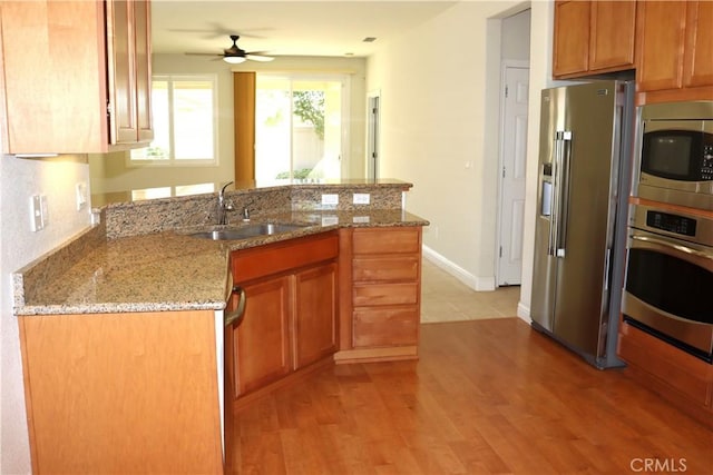 1573 Maple Valley St, Manteca, CA 95336 - kitchen with stainless steel appliances, a peninsula, light wood-style flooring, a ceiling fan, and brown cabinetry