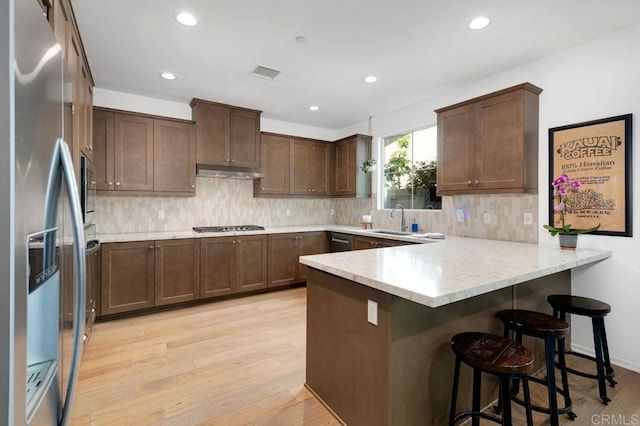 140 Unity Ln, San Marcos, CA 92078 - kitchen with appliances with stainless steel finishes, under cabinet range hood, a peninsula, light wood-type flooring, and backsplash