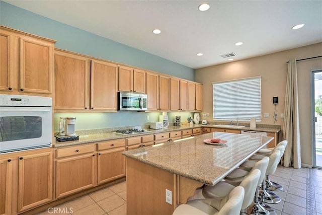 82756 Burnette Dr, Indio, CA 92201 - kitchen featuring oven, stainless steel microwave, light tile patterned flooring, a kitchen bar, and recessed lighting