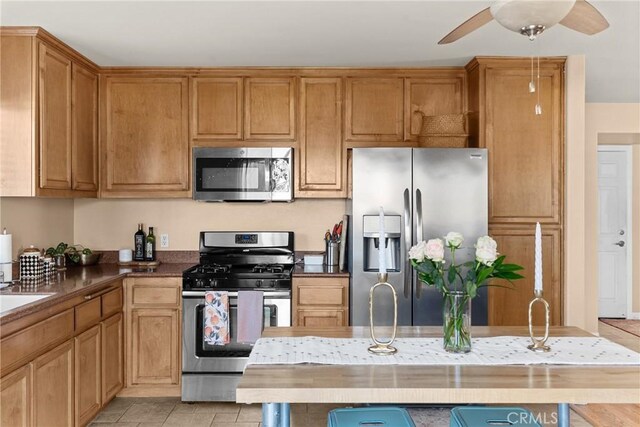249 Colt Ln, Nipomo, CA 93444 - kitchen featuring appliances with stainless steel finishes, a ceiling fan, light tile patterned floors, dark countertops, and brown cabinets
