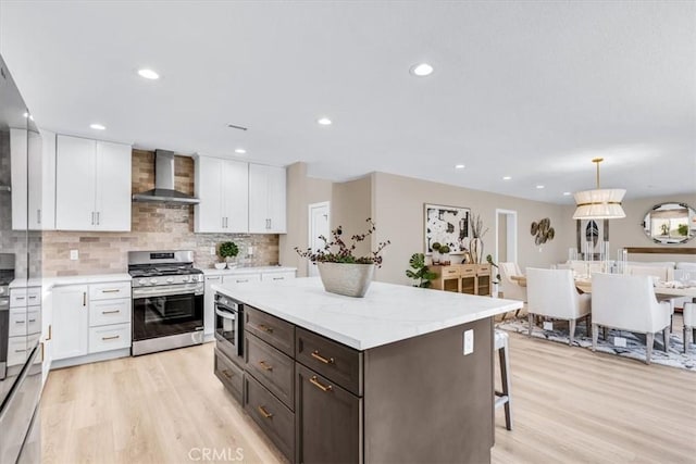 22461 Silver Spur, Lake Forest, CA 92630 - kitchen with stainless steel range with gas cooktop, wall chimney range hood, white cabinetry, light wood-style flooring, and backsplash