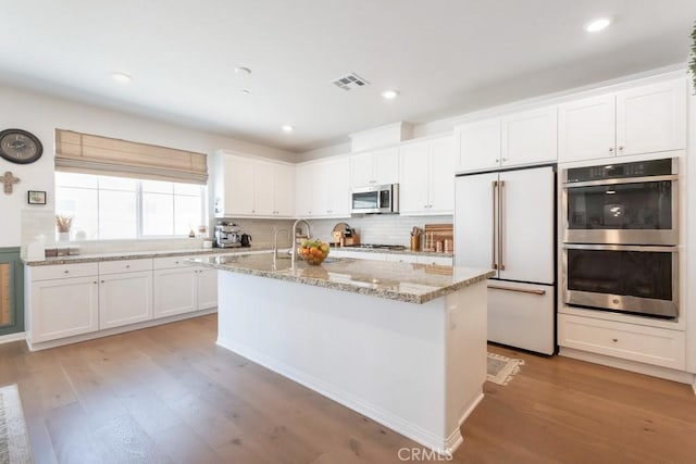 874 Royal Knight Trl, Redlands, CA 92374 - kitchen with stainless steel appliances, white cabinets, light wood-type flooring, light stone counters, and a kitchen island with sink