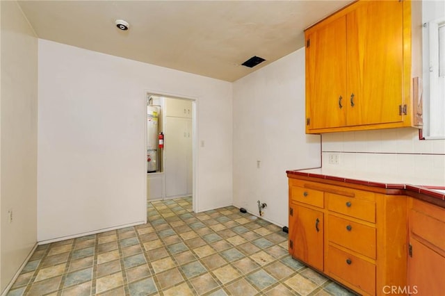 11701 Roseglen St, El Monte, CA 91732 - kitchen featuring tile counters, stone finish floors, brown cabinetry, and decorative backsplash