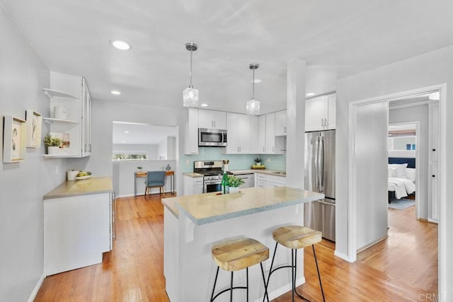 3833 Tomahawk Ln, San Diego, CA 92117 - kitchen with appliances with stainless steel finishes, white cabinets, a kitchen breakfast bar, light wood-style flooring, and recessed lighting
